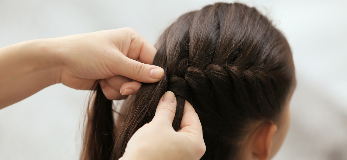 Visuel d'une petite fille brune de dos en train de se faire tresser les cheveux
